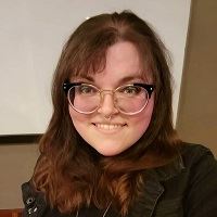 A smiling woman with shoulder length mahogany brown hair and glasses.