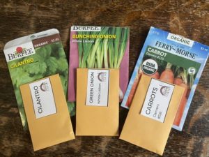 Three varieties of seed packets on a tabletop with manila envelopes ready for notes.